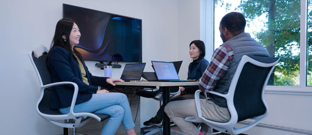 Three people sitting in conference room with screens